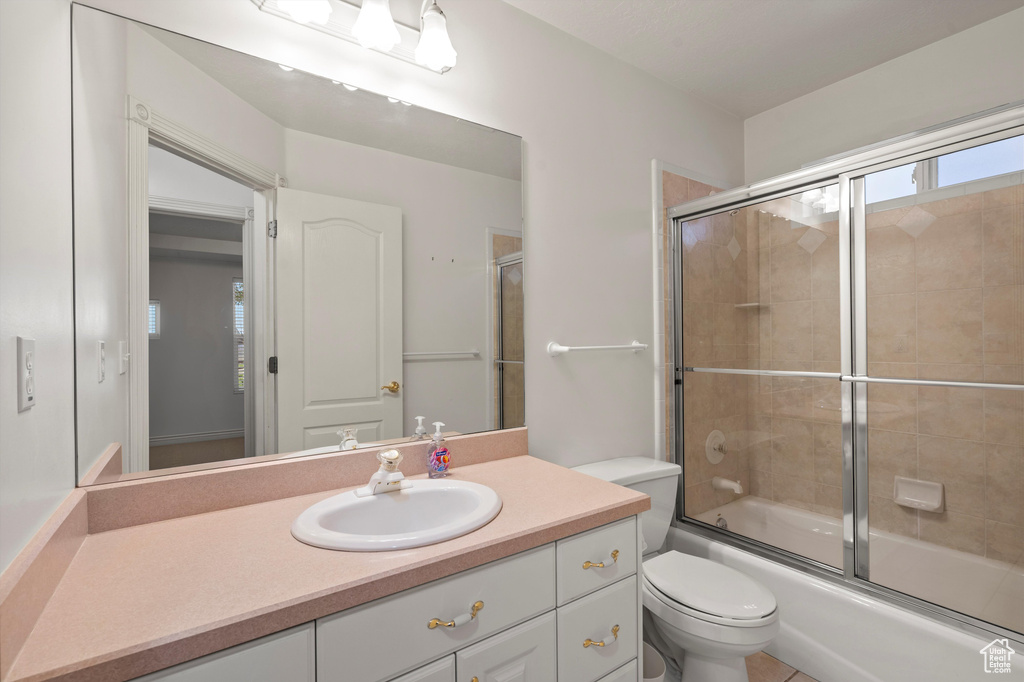 Bathroom with toilet, vanity, and bath / shower combo with glass door