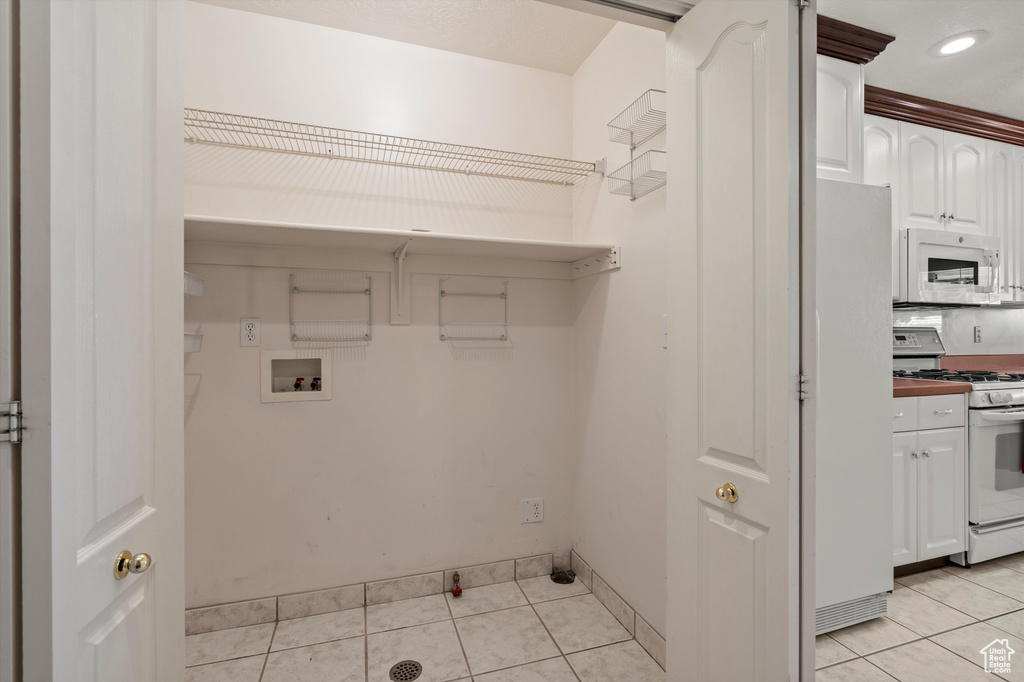 Laundry area with hookup for a washing machine, light tile patterned floors, and baseboards