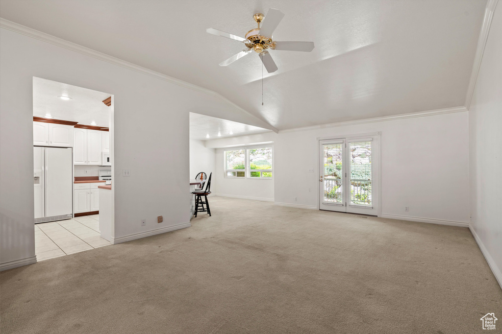 Unfurnished living room featuring light colored carpet, crown molding, ceiling fan, vaulted ceiling, and baseboards