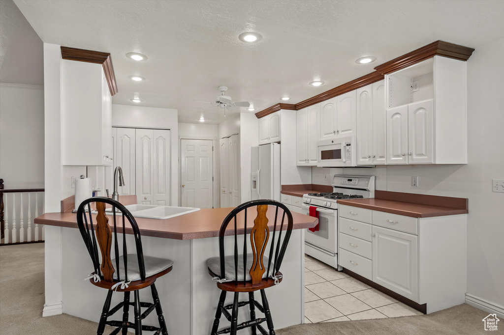 Kitchen with white appliances, a kitchen breakfast bar, dark countertops, a peninsula, and white cabinetry