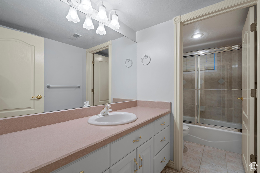 Full bath featuring toilet, tile patterned flooring, vanity, and combined bath / shower with glass door