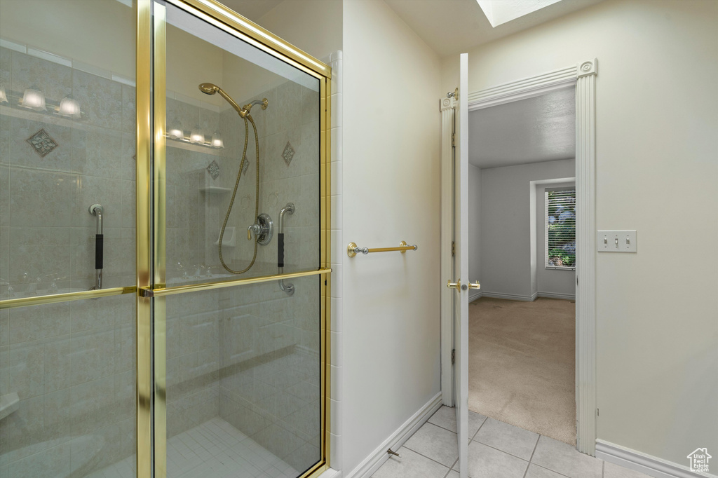Full bath with a shower stall, baseboards, tile patterned flooring, and a skylight