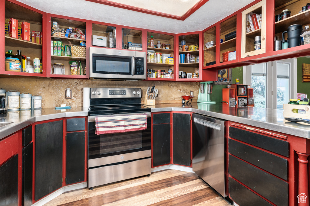 Kitchen with stainless steel appliances, open shelves, backsplash, light wood finished floors, and light countertops