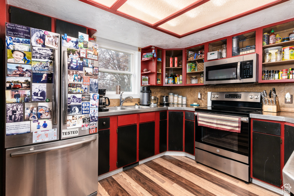 Kitchen featuring appliances with stainless steel finishes, stainless steel countertops, a sink, open shelves, and light wood-style floors