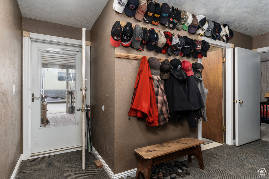 Doorway featuring carpet, a textured wall, and baseboards