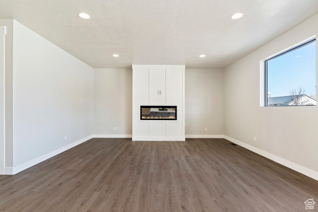 Unfurnished living room featuring recessed lighting, wood finished floors, baseboards, and a glass covered fireplace
