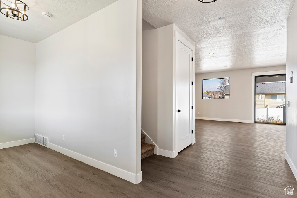 Unfurnished room with wood finished floors, baseboards, a chandelier, a textured ceiling, and stairway
