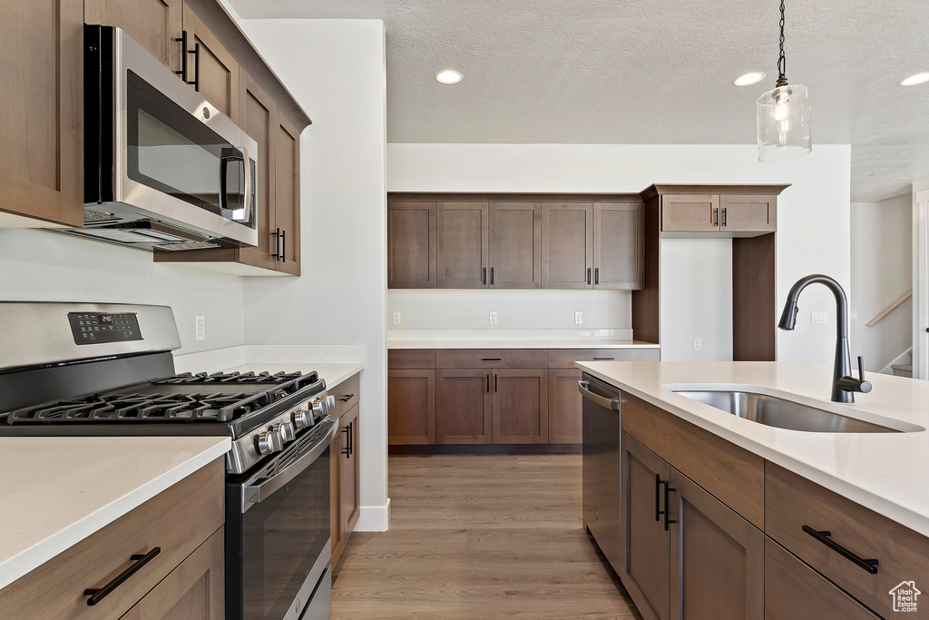 Kitchen with appliances with stainless steel finishes, a sink, light wood-type flooring, light countertops, and pendant lighting