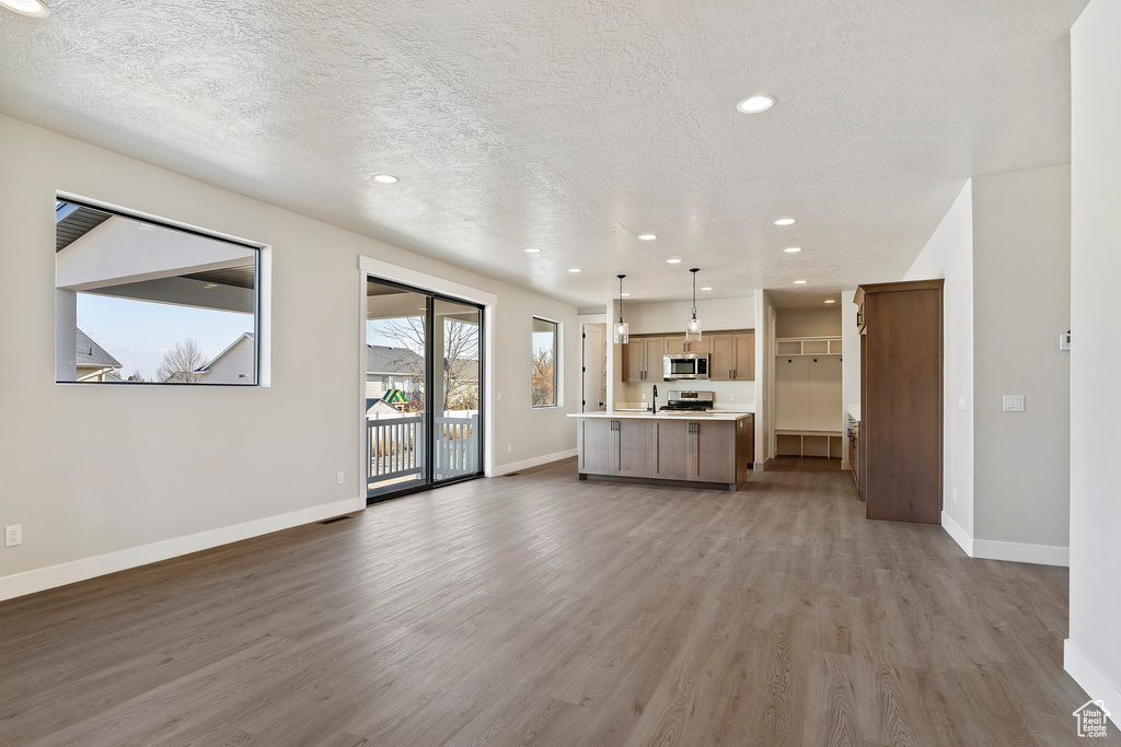 Kitchen featuring stainless steel appliances, open floor plan, wood finished floors, baseboards, and light countertops