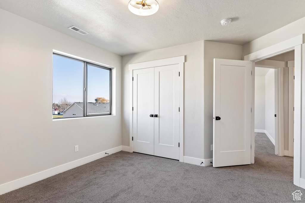 Unfurnished bedroom with carpet flooring, a textured ceiling, baseboards, and a closet