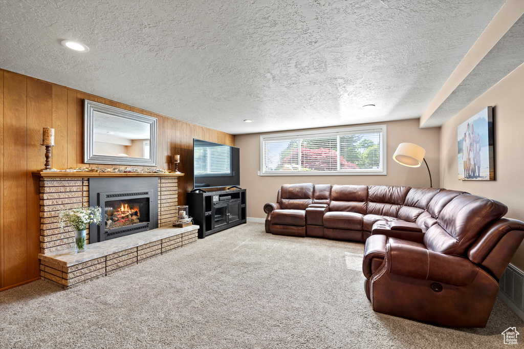 Carpeted living room featuring a textured ceiling, a brick fireplace, and wood walls