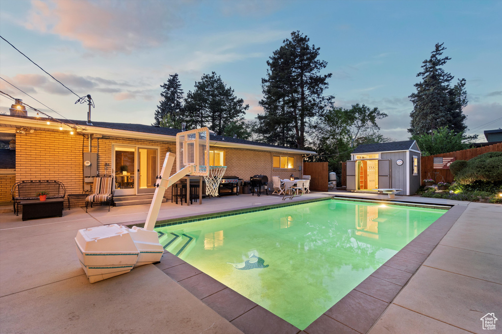 Pool at dusk featuring a patio area, a shed, fence, an outbuilding, and an outdoor hangout area