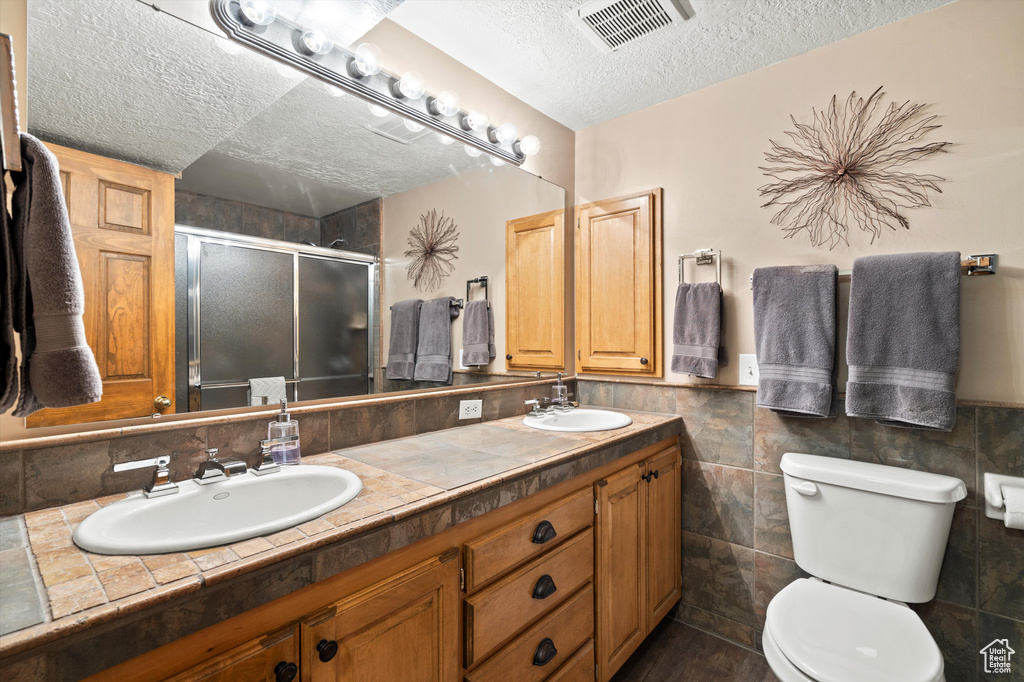Bathroom with a textured ceiling, a stall shower, toilet, double vanity, and tile walls