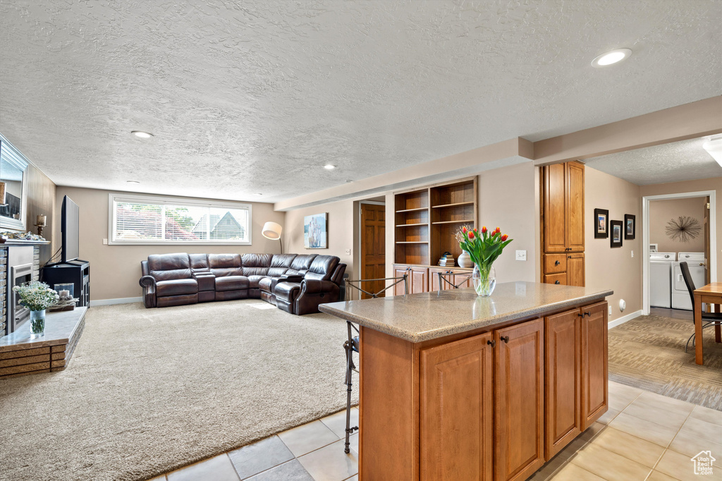 Kitchen featuring washing machine and clothes dryer, a textured ceiling, baseboards, a kitchen breakfast bar, and a center island