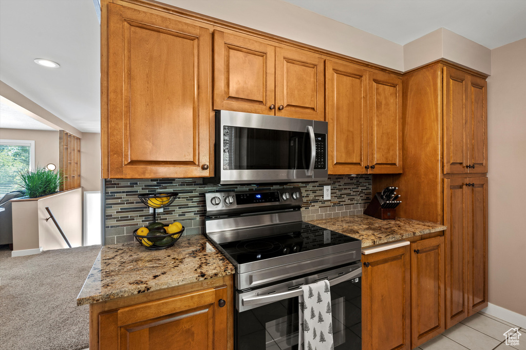 Kitchen with appliances with stainless steel finishes, brown cabinets, backsplash, and light stone countertops
