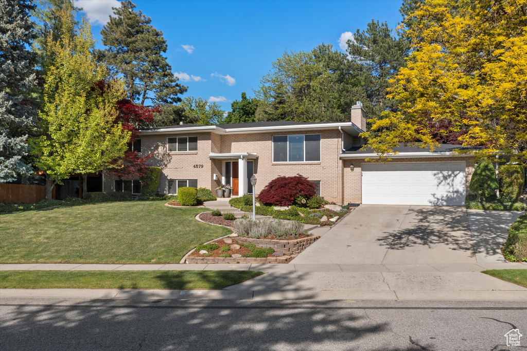 View of front facade with driveway, a front yard, brick siding, a chimney, and a garage