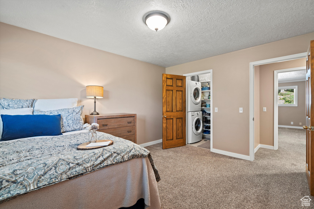 Carpeted bedroom with stacked washer and clothes dryer, baseboards, and a textured ceiling
