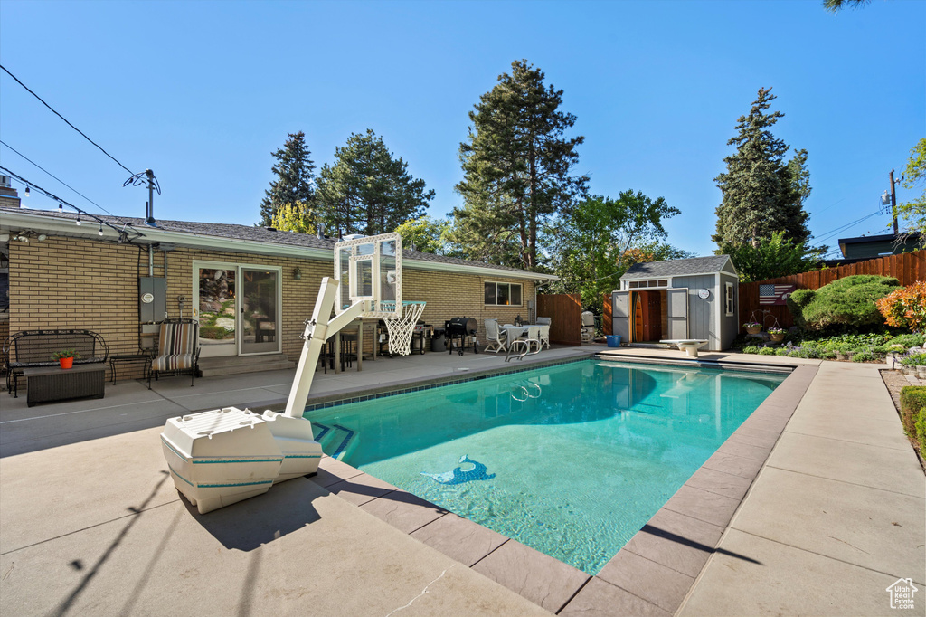 View of swimming pool with a patio, a shed, fence, an outbuilding, and a diving board