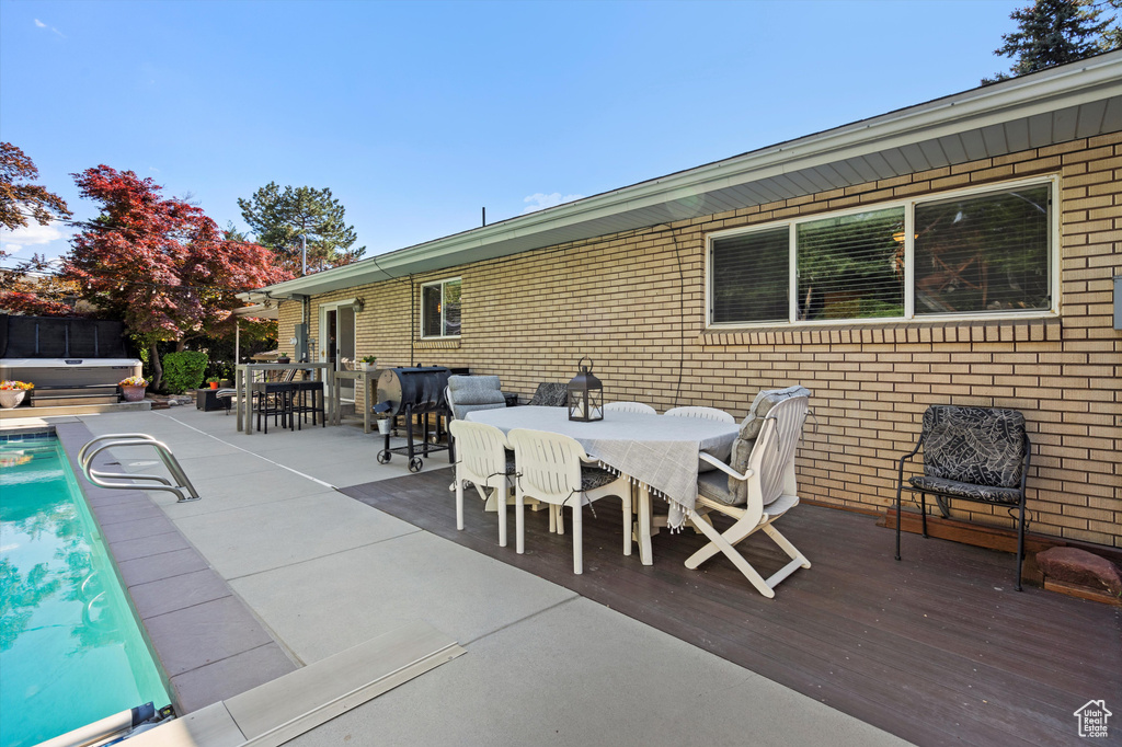 View of patio / terrace featuring outdoor dining area, a hot tub, a wooden deck, and an outdoor pool