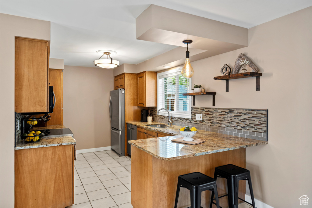 Kitchen with a sink, freestanding refrigerator, a peninsula, brown cabinets, and decorative backsplash