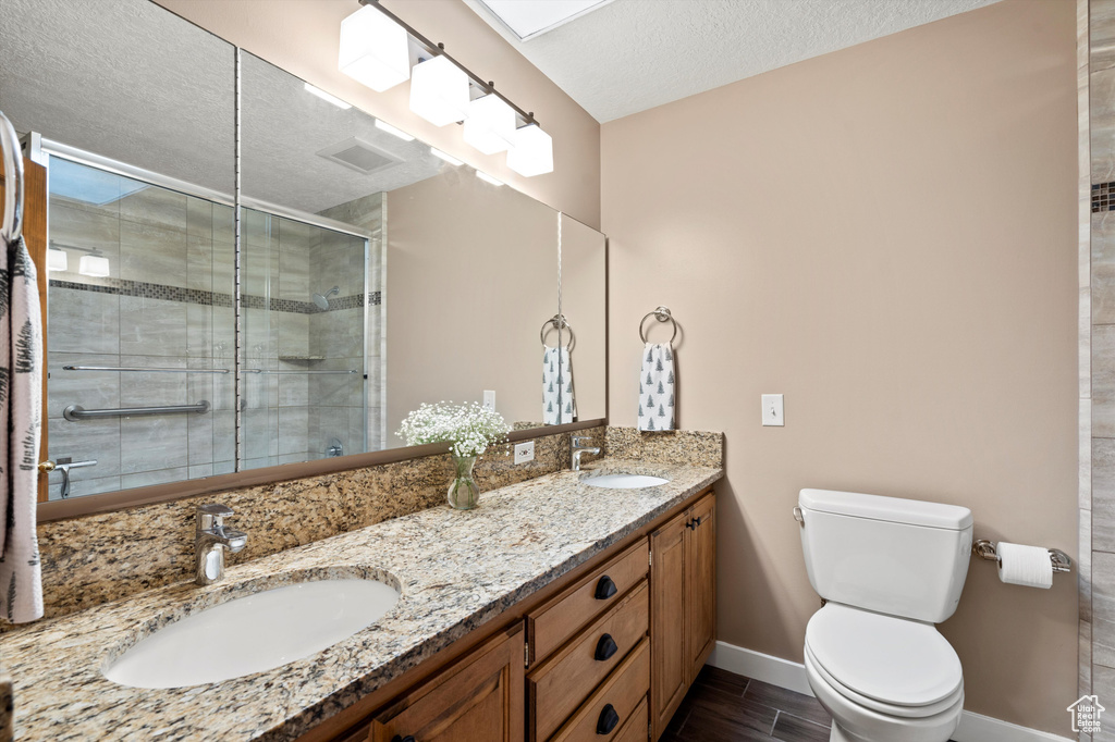 Bathroom featuring toilet, a shower stall, baseboards, a textured ceiling, and double vanity