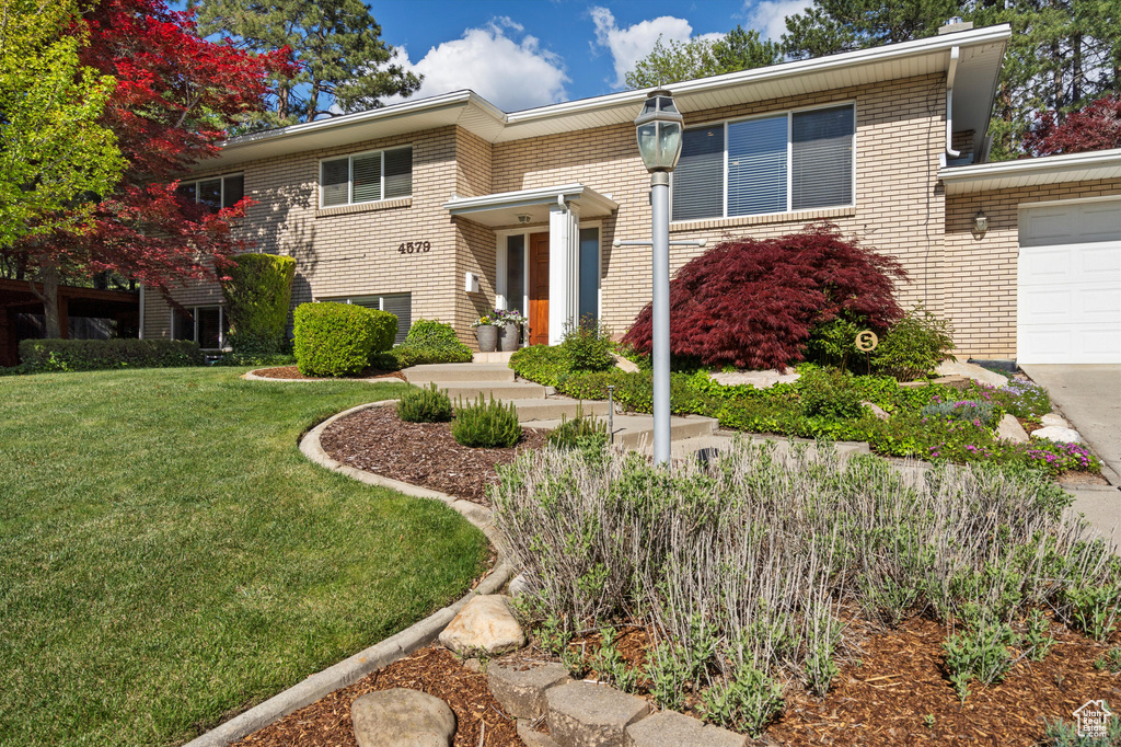 View of front of property with brick siding, a front yard, an attached garage, and driveway