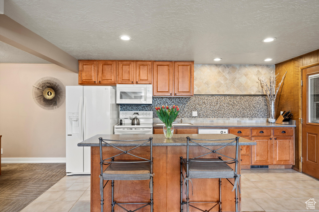 Kitchen with white appliances, brown cabinetry, a breakfast bar, decorative backsplash, and recessed lighting