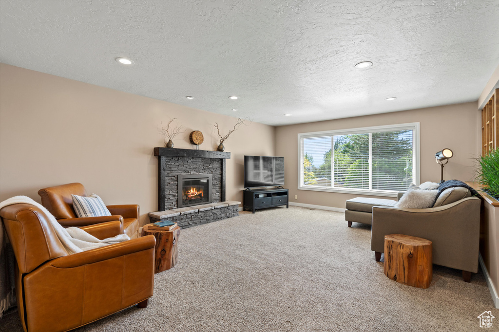 Carpeted living area featuring a textured ceiling, a stone fireplace, recessed lighting, and baseboards
