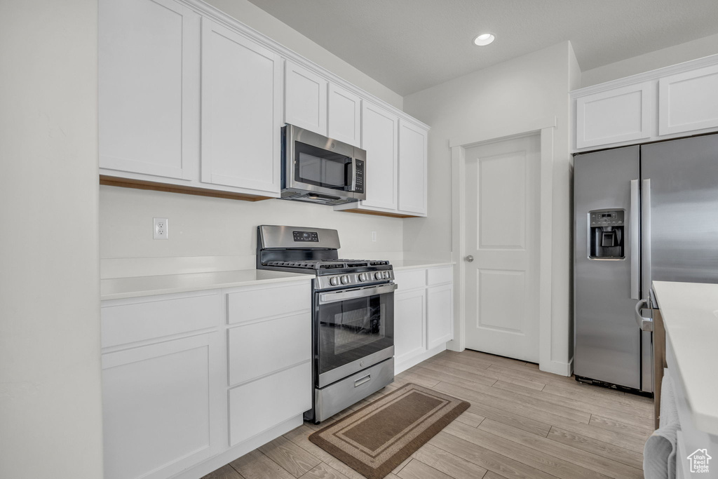 Kitchen featuring appliances with stainless steel finishes, light wood-style floors, white cabinets, light countertops, and recessed lighting