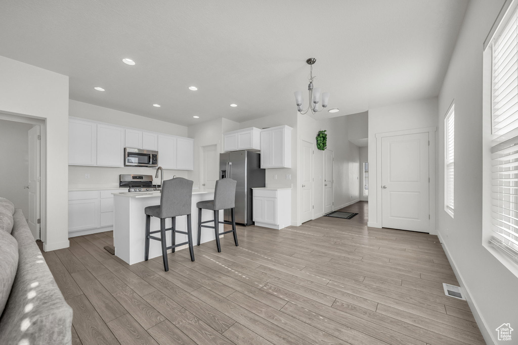 Kitchen featuring stainless steel appliances, light wood finished floors, recessed lighting, a breakfast bar, and white cabinetry