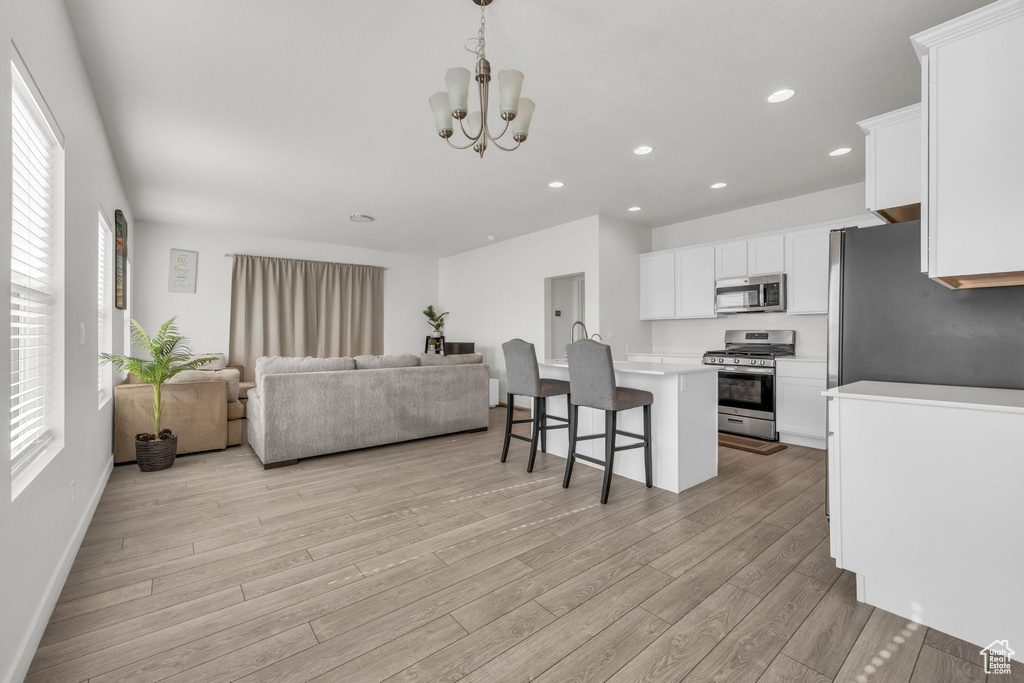 Kitchen with stainless steel appliances, open floor plan, a breakfast bar, light wood-style floors, and light countertops