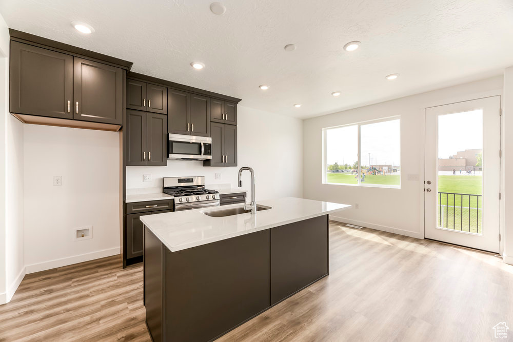 Kitchen with appliances with stainless steel finishes, a sink, light wood finished floors, baseboards, and light countertops