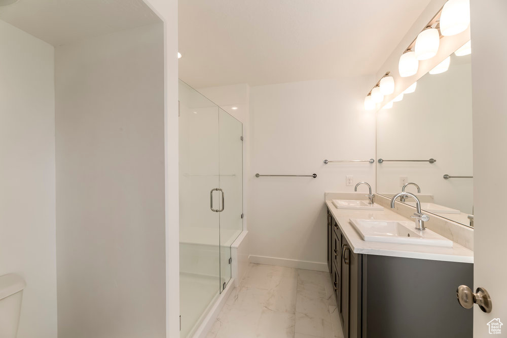 Bathroom featuring marble finish flooring, a stall shower, double vanity, toilet, and baseboards