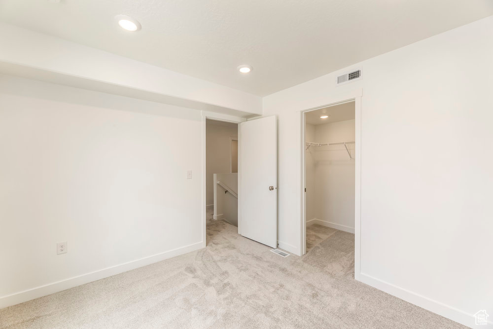 Unfurnished bedroom featuring recessed lighting, light carpet, baseboards, a walk in closet, and a closet
