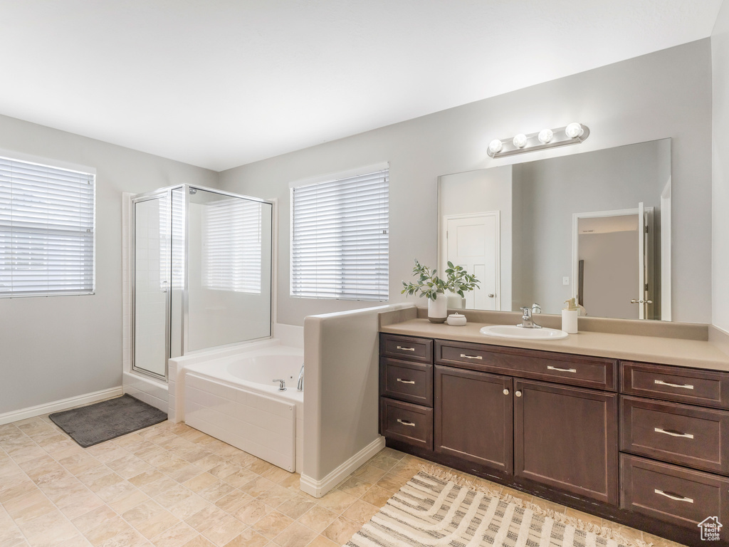 Bathroom featuring a shower stall, vanity, a garden tub, and baseboards