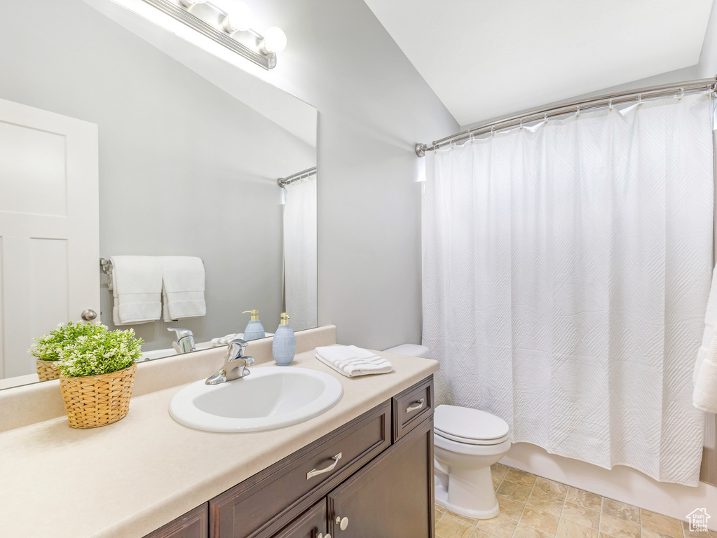 Bathroom featuring toilet, lofted ceiling, vanity, and shower / bath combo with shower curtain