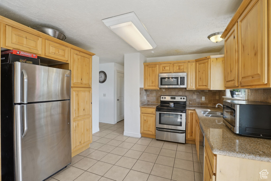 Kitchen featuring stainless steel appliances, decorative backsplash, a sink, light tile patterned floors, and light stone counters