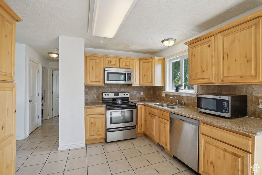 Kitchen with appliances with stainless steel finishes, a sink, light tile patterned floors, light brown cabinetry, and a textured ceiling