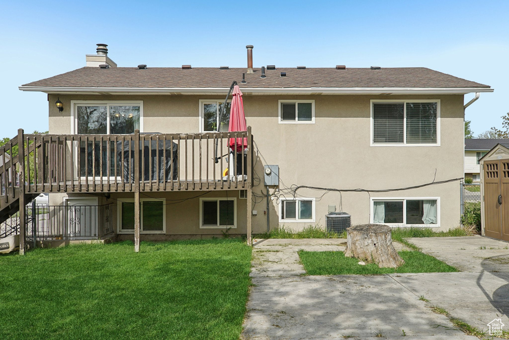 Rear view of property with stucco siding, a wooden deck, a lawn, and a chimney
