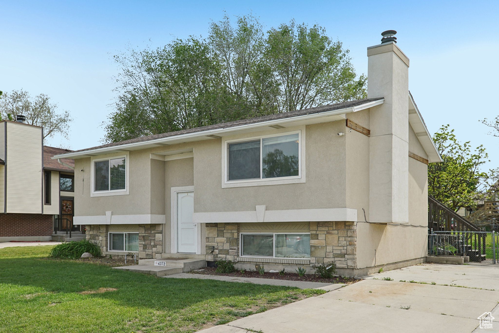 View of front of home with stone siding, a front lawn, a chimney, and stucco siding