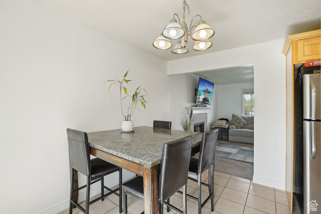 Dining space with a chandelier, light tile patterned flooring, baseboards, a fireplace, and a textured ceiling
