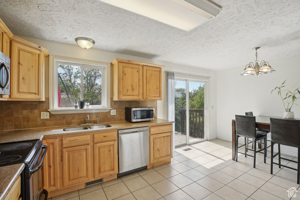Kitchen with stainless steel appliances, a sink, backsplash, a chandelier, and light tile patterned floors