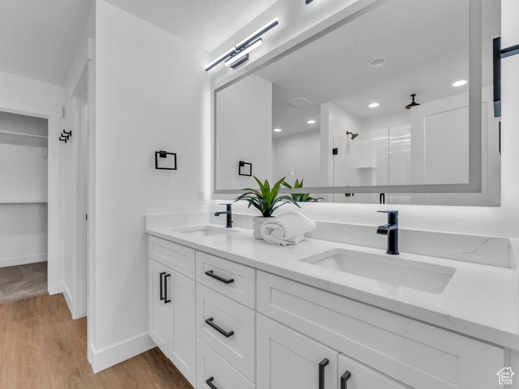 Bathroom with wood finished floors, walk in shower, double vanity, baseboards, and recessed lighting