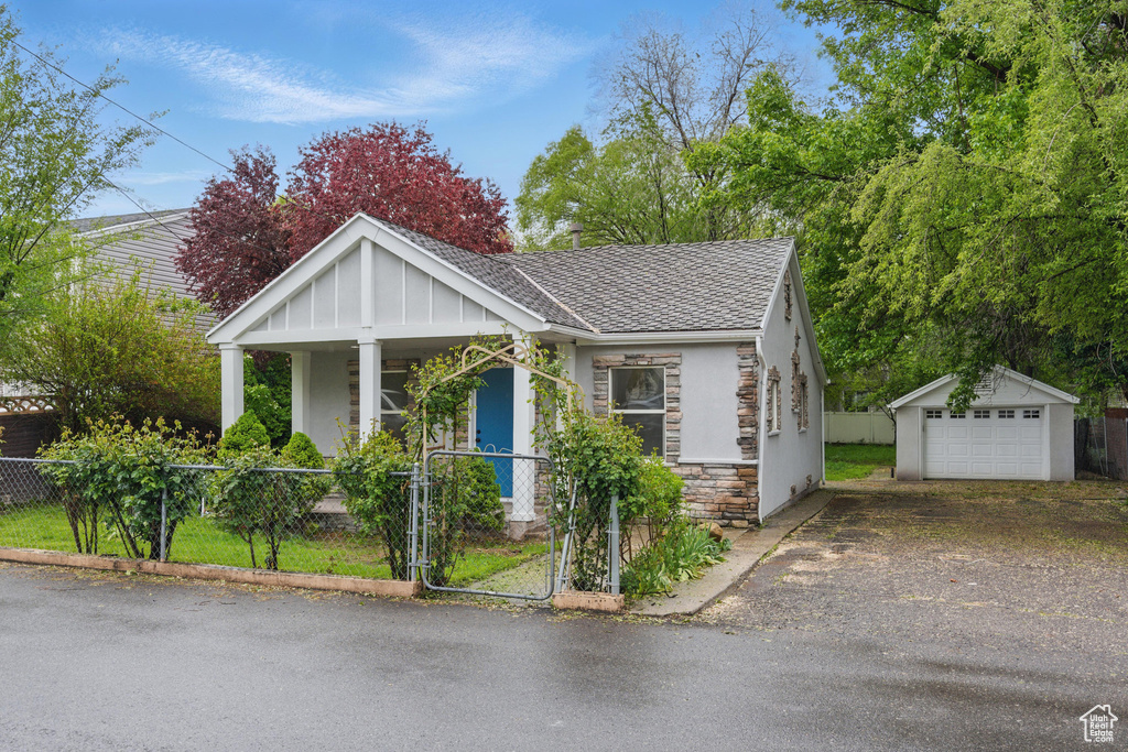 Bungalow with a fenced front yard, stone siding, an outdoor structure, and a garage