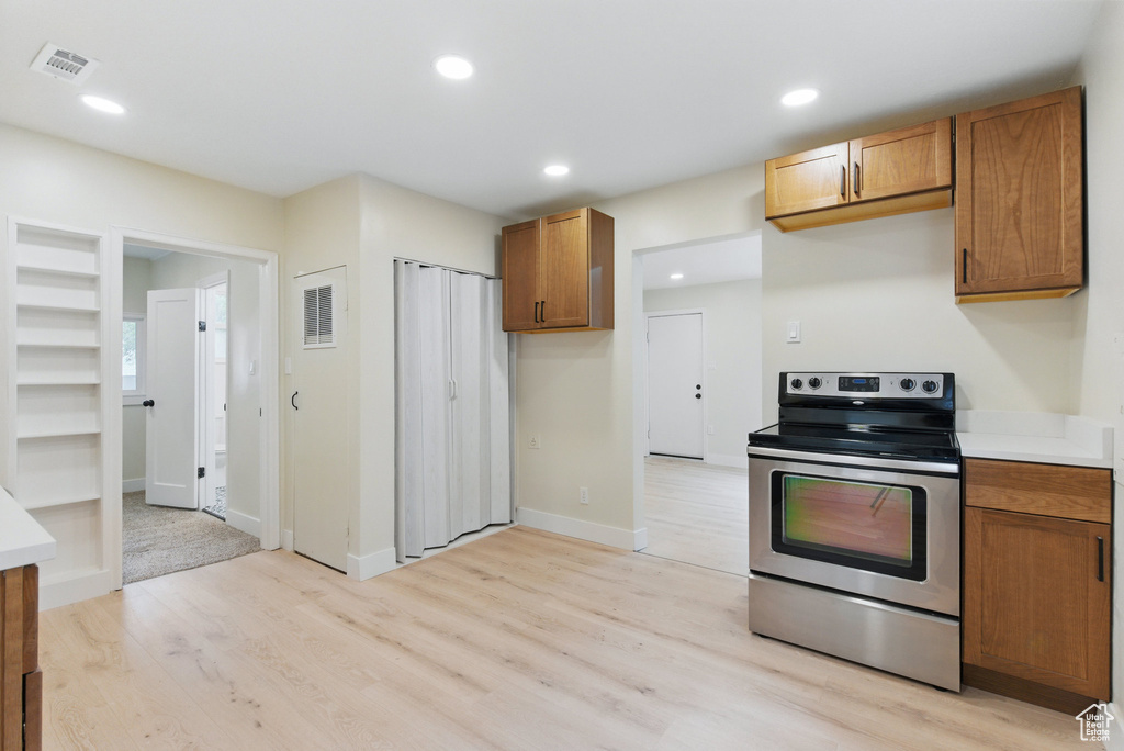 Kitchen featuring stainless steel range with electric cooktop, light wood finished floors, brown cabinetry, light countertops, and recessed lighting