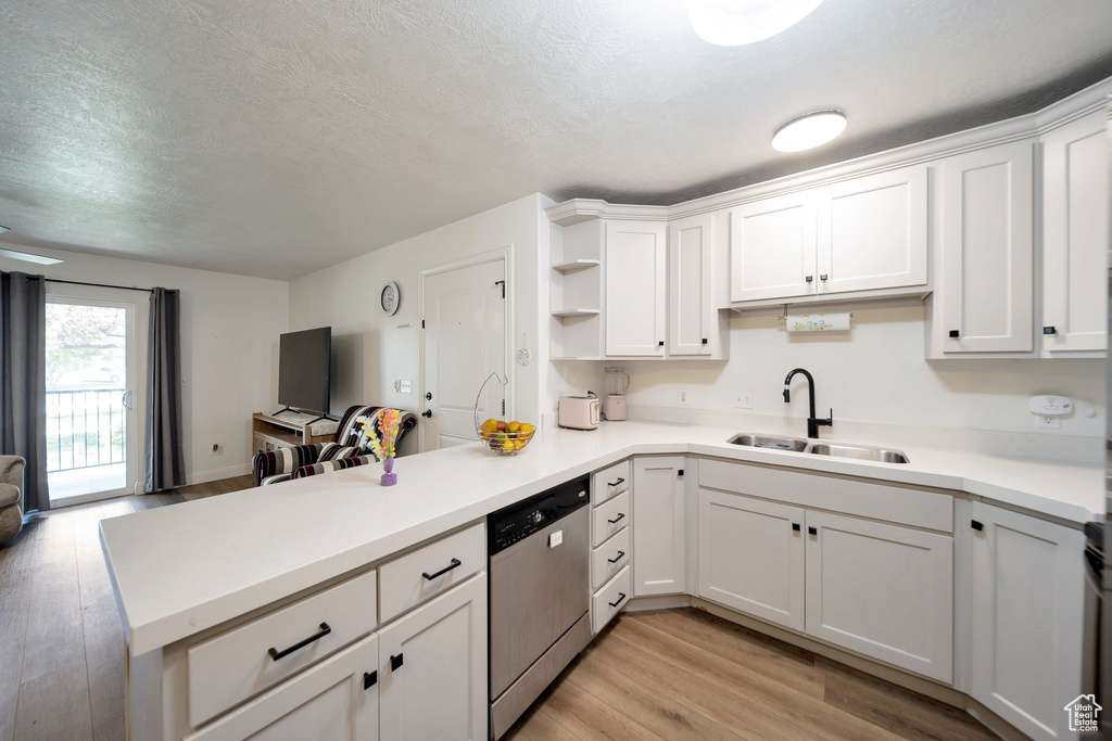 Kitchen with stainless steel dishwasher, a peninsula, a sink, light wood-type flooring, and a textured ceiling