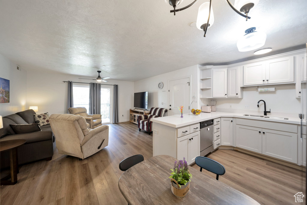 Kitchen with a sink, stainless steel dishwasher, open floor plan, white cabinetry, and light countertops