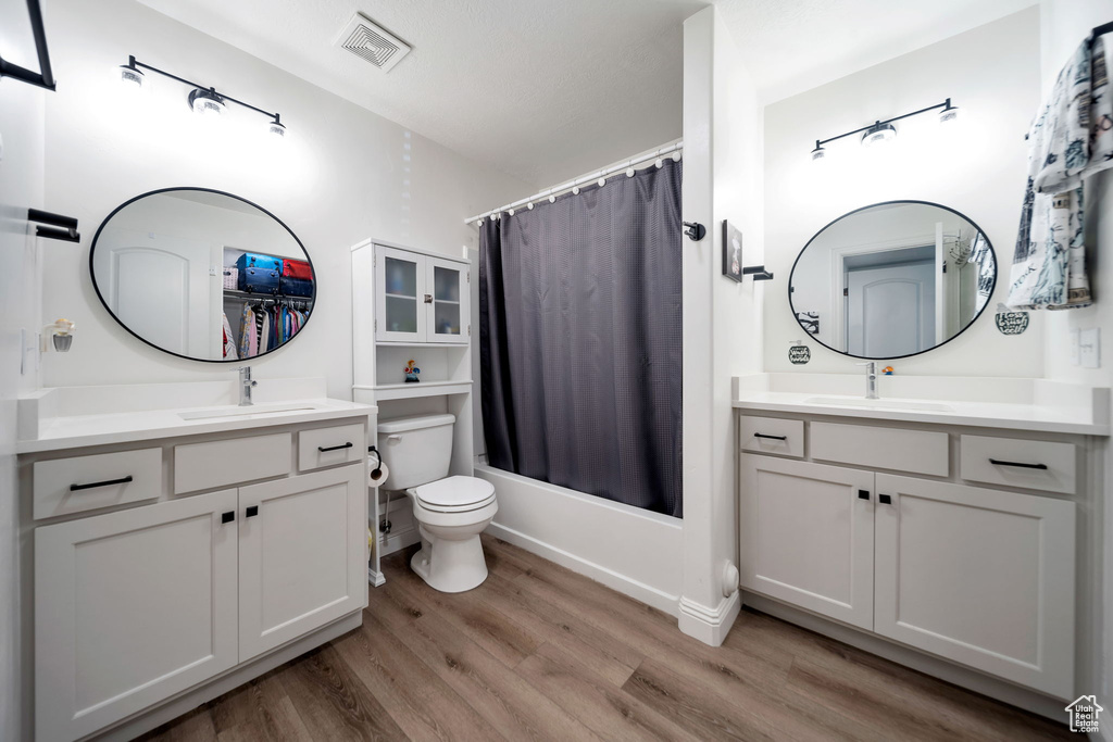 Bathroom featuring wood finished floors, toilet, two vanities, and shower / tub combo
