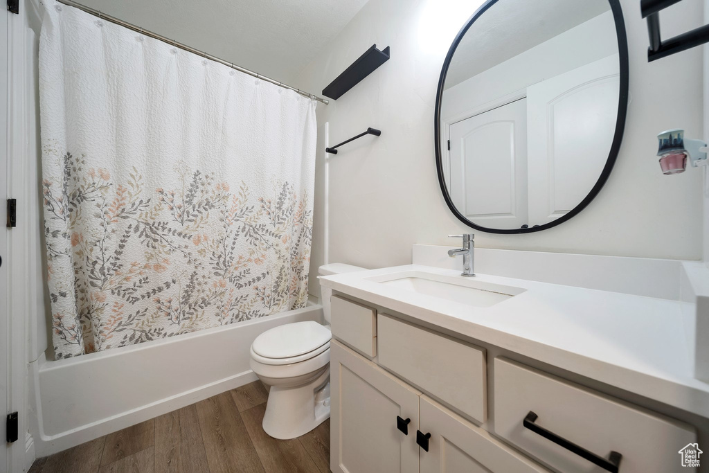 Bathroom featuring wood finished floors, toilet, vanity, and shower / bathtub combination with curtain