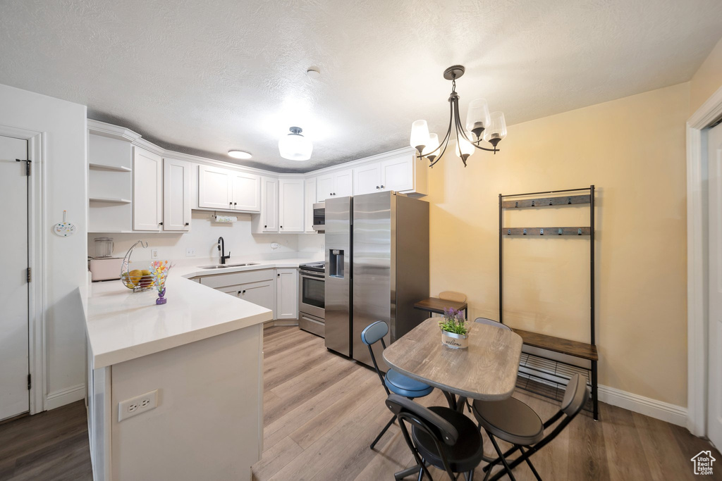 Kitchen featuring appliances with stainless steel finishes, white cabinetry, light countertops, and light wood finished floors